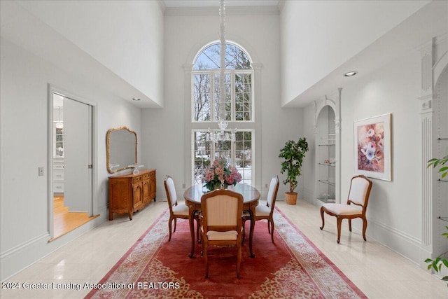 dining space with tile patterned flooring, ornamental molding, a high ceiling, and an inviting chandelier