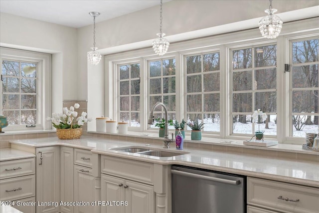 kitchen featuring stainless steel dishwasher, decorative light fixtures, light stone countertops, and sink