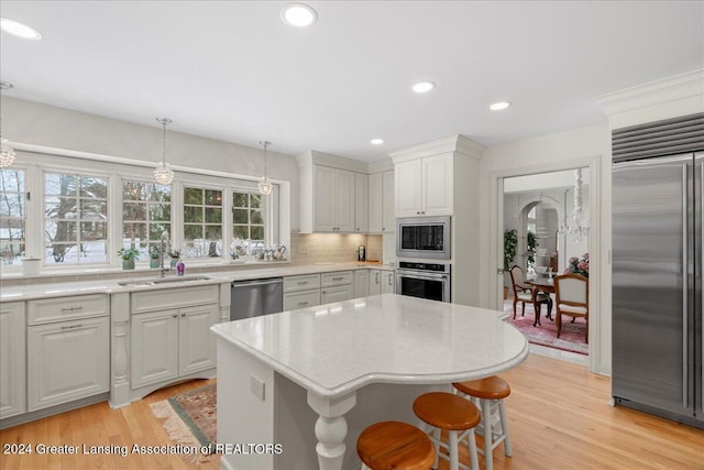 kitchen with sink, built in appliances, light hardwood / wood-style flooring, a kitchen island, and hanging light fixtures