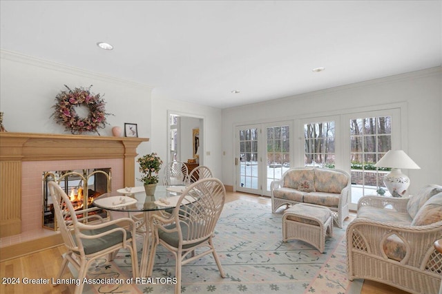 dining space with a tile fireplace, french doors, light wood-type flooring, and crown molding