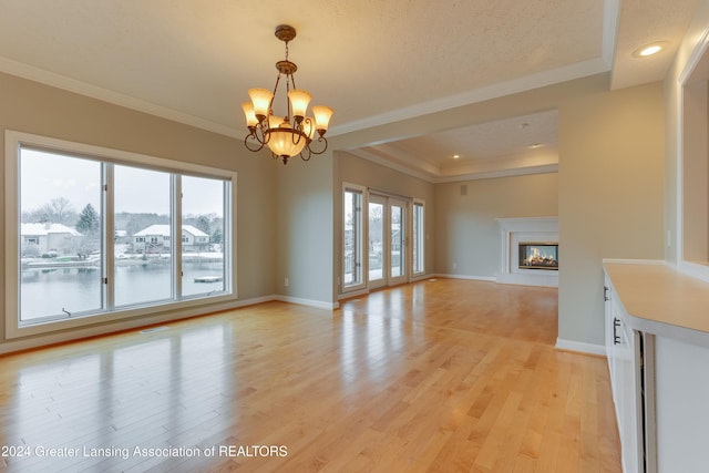 unfurnished living room with a raised ceiling, ornamental molding, a chandelier, and light hardwood / wood-style floors