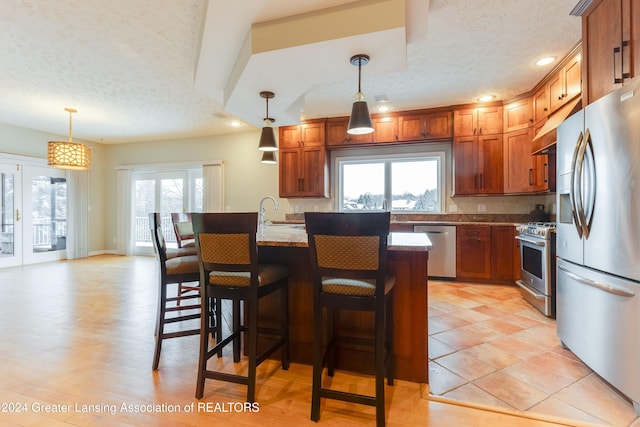 kitchen with light stone counters, hanging light fixtures, plenty of natural light, and stainless steel appliances