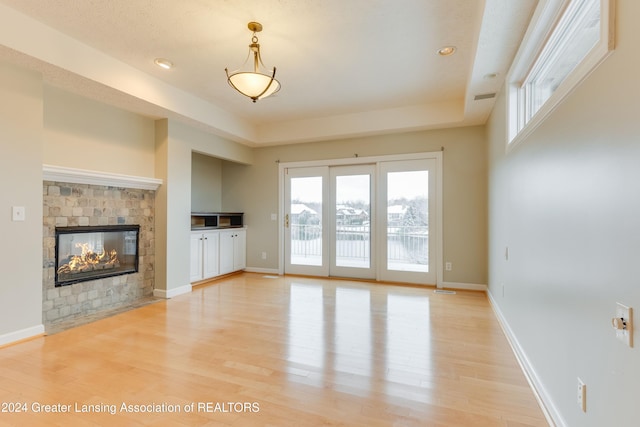 unfurnished living room featuring a tray ceiling, light wood-type flooring, and a multi sided fireplace