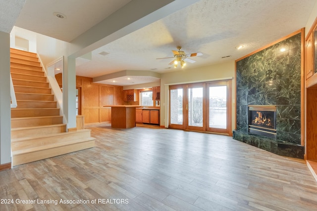 unfurnished living room featuring light wood-type flooring, a textured ceiling, a fireplace, and ceiling fan