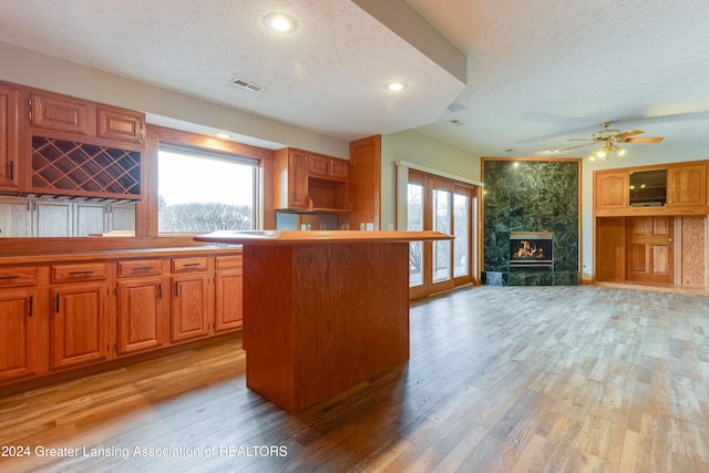 kitchen featuring a center island, a textured ceiling, light wood-type flooring, ceiling fan, and a high end fireplace