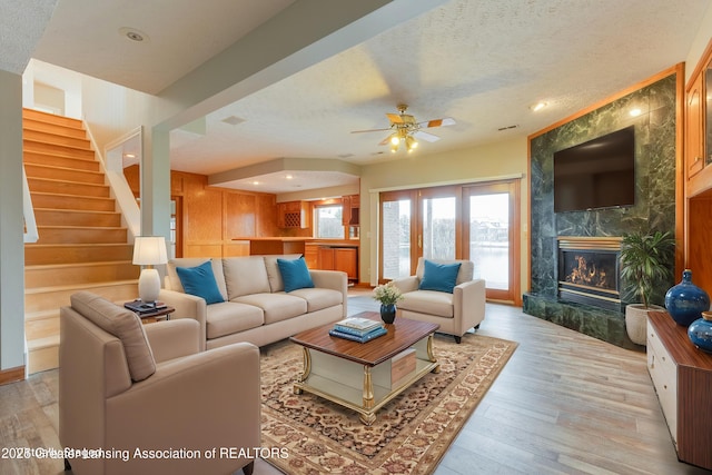 living room featuring ceiling fan, a textured ceiling, a fireplace, and light hardwood / wood-style flooring