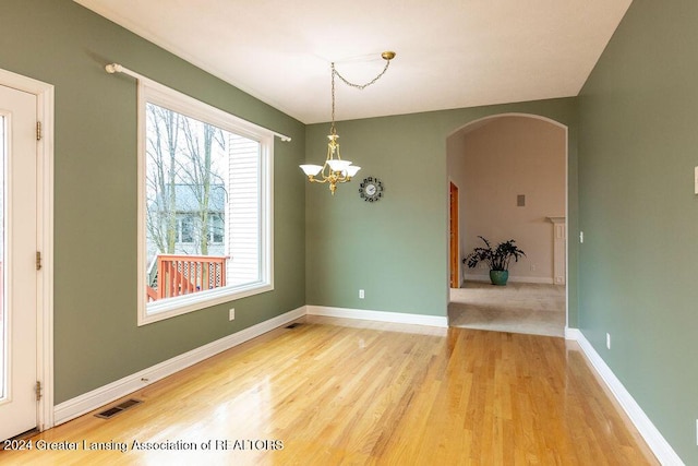 spare room with hardwood / wood-style floors, an inviting chandelier, and a healthy amount of sunlight