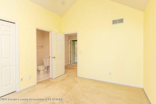 unfurnished bedroom with high vaulted ceiling, light colored carpet, and connected bathroom