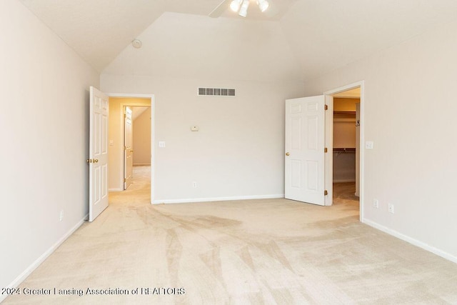 unfurnished bedroom featuring light carpet, a walk in closet, vaulted ceiling, ceiling fan, and a closet