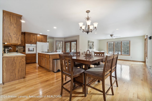 dining area featuring ceiling fan with notable chandelier, sink, and light hardwood / wood-style flooring