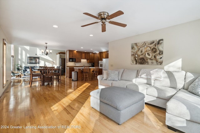 living room featuring ceiling fan with notable chandelier and light hardwood / wood-style flooring