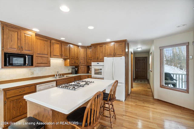 kitchen with white appliances, backsplash, a kitchen island, light hardwood / wood-style floors, and a breakfast bar area