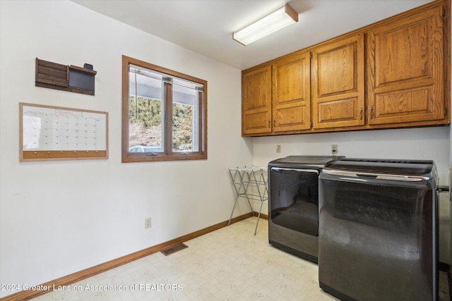 clothes washing area with separate washer and dryer and cabinets