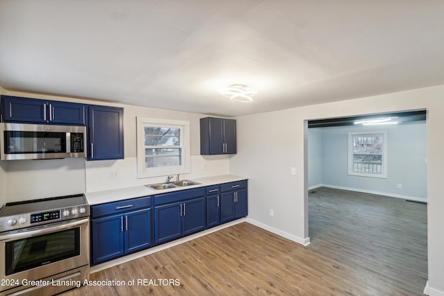 kitchen with sink, hardwood / wood-style floors, blue cabinets, and appliances with stainless steel finishes