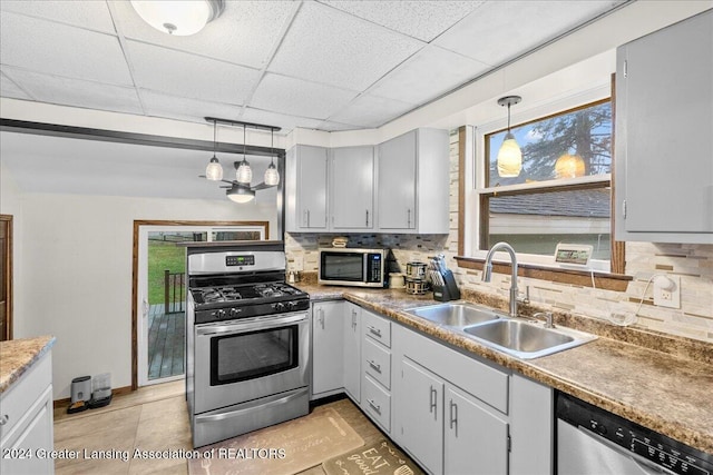 kitchen with tasteful backsplash, a drop ceiling, stainless steel appliances, sink, and hanging light fixtures