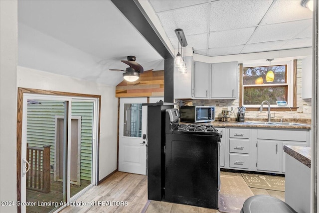 kitchen with sink, a drop ceiling, pendant lighting, decorative backsplash, and light wood-type flooring