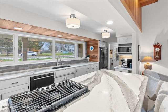 kitchen with light stone countertops, sink, backsplash, white cabinets, and appliances with stainless steel finishes