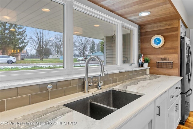 kitchen featuring light stone countertops, stainless steel refrigerator, wooden ceiling, and sink