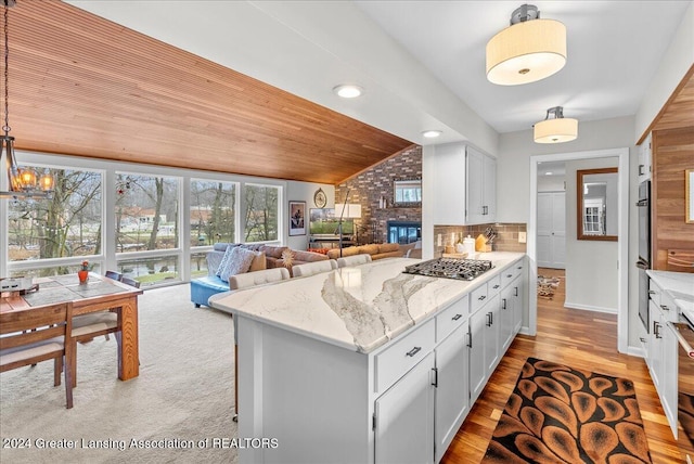 kitchen with white cabinetry, hanging light fixtures, wooden ceiling, backsplash, and a fireplace