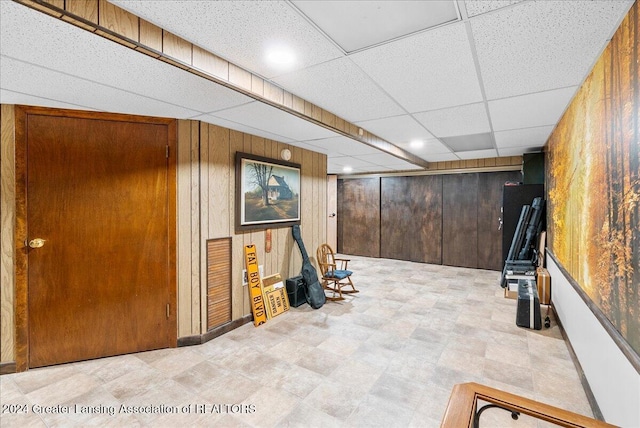 basement with a drop ceiling and wood walls