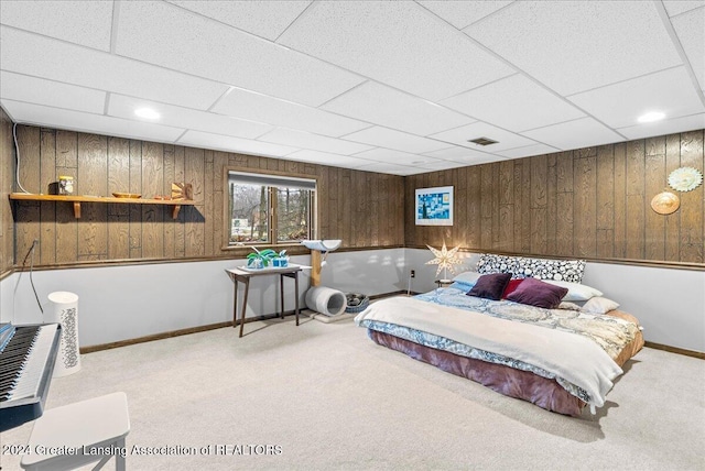 carpeted bedroom featuring a paneled ceiling and wooden walls