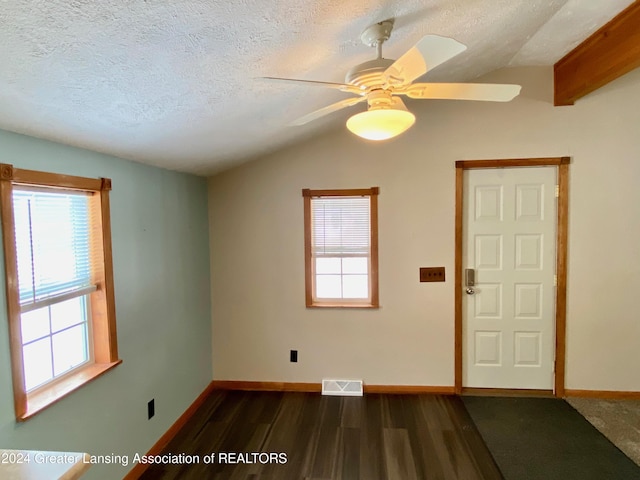 empty room with a textured ceiling, lofted ceiling with beams, dark hardwood / wood-style floors, and ceiling fan