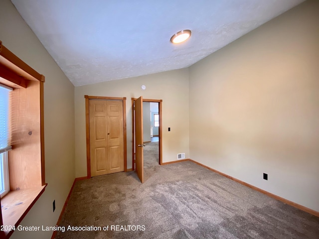 unfurnished room with carpet flooring, lofted ceiling, and a healthy amount of sunlight