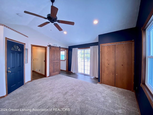 unfurnished bedroom with carpet flooring, a barn door, ceiling fan, and vaulted ceiling