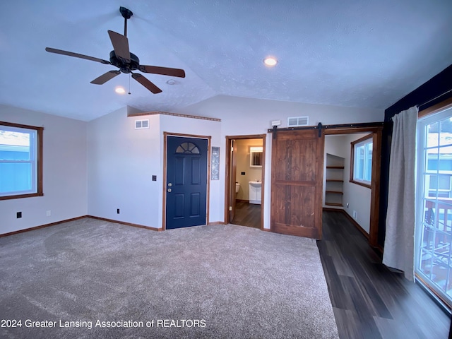 interior space with lofted ceiling, ceiling fan, a barn door, a textured ceiling, and dark hardwood / wood-style flooring