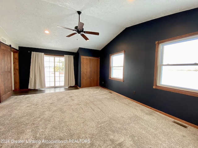 unfurnished bedroom with a barn door, vaulted ceiling, multiple windows, and ceiling fan