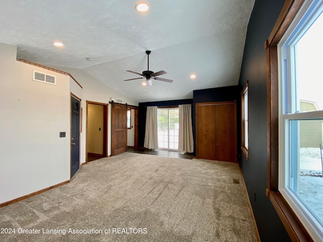 unfurnished bedroom featuring carpet flooring, a barn door, a textured ceiling, and lofted ceiling