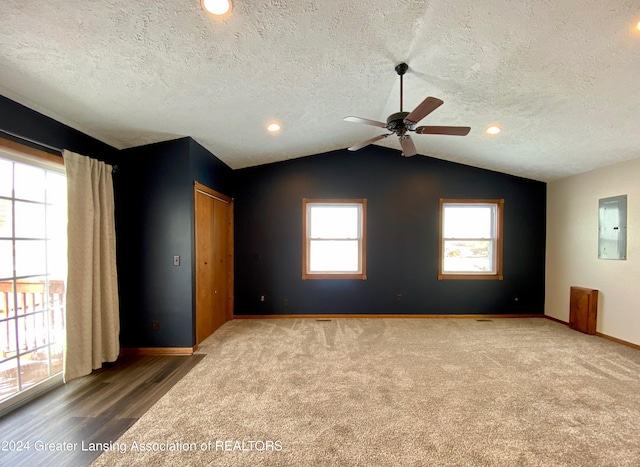 spare room with a textured ceiling, ceiling fan, wood-type flooring, electric panel, and lofted ceiling