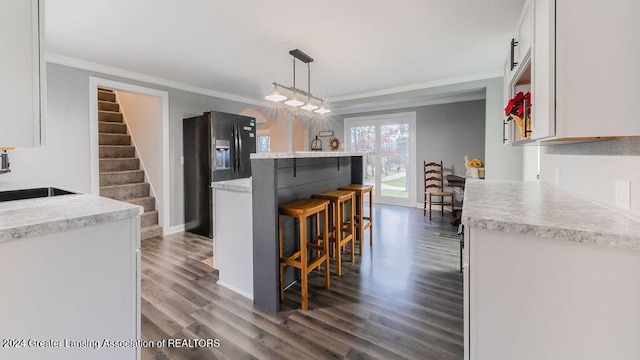 kitchen featuring dark wood-type flooring, white cabinets, black fridge, sink, and decorative light fixtures