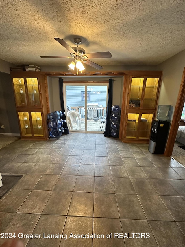 unfurnished living room featuring a textured ceiling, dark tile patterned flooring, and ceiling fan