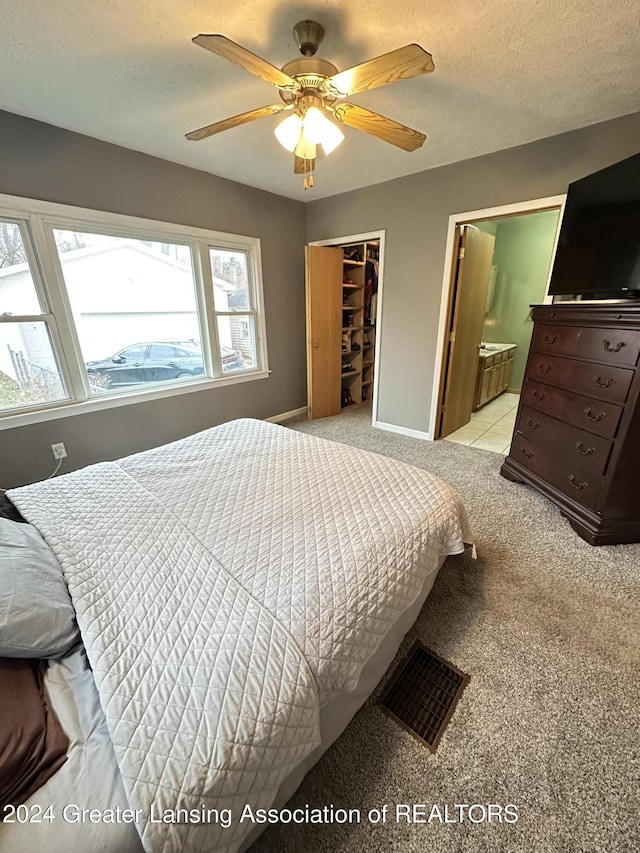 carpeted bedroom featuring a walk in closet, a textured ceiling, ceiling fan, connected bathroom, and a closet