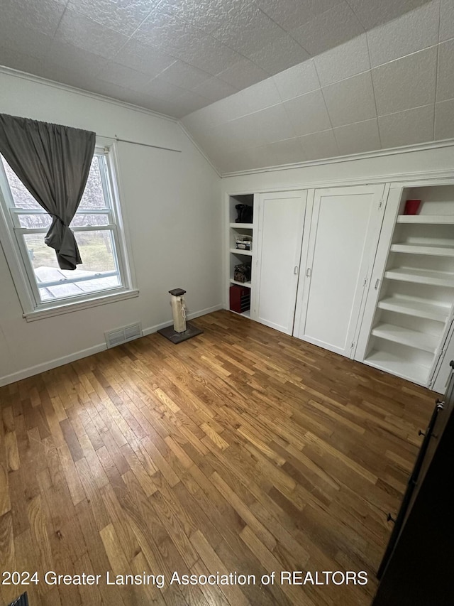 additional living space with built in shelves, wood-type flooring, and vaulted ceiling