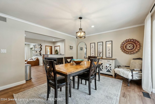 dining space featuring hardwood / wood-style floors, a stone fireplace, and ornamental molding