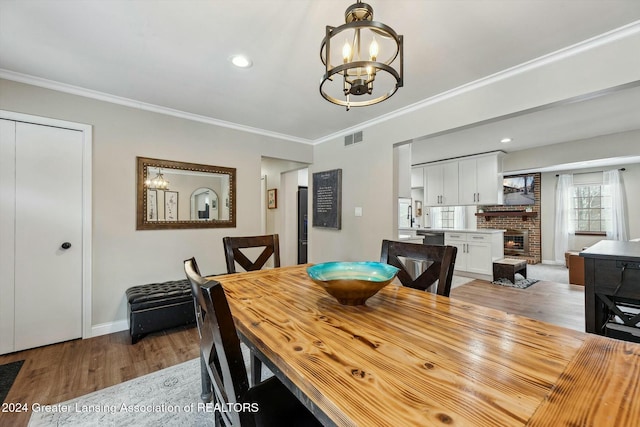 dining area featuring hardwood / wood-style flooring, ornamental molding, a fireplace, and an inviting chandelier