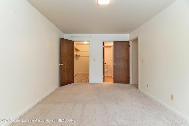 unfurnished bedroom with a walk in closet, light carpet, connected bathroom, and a closet