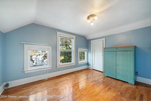 unfurnished bedroom with hardwood / wood-style floors, lofted ceiling, a textured ceiling, and a closet