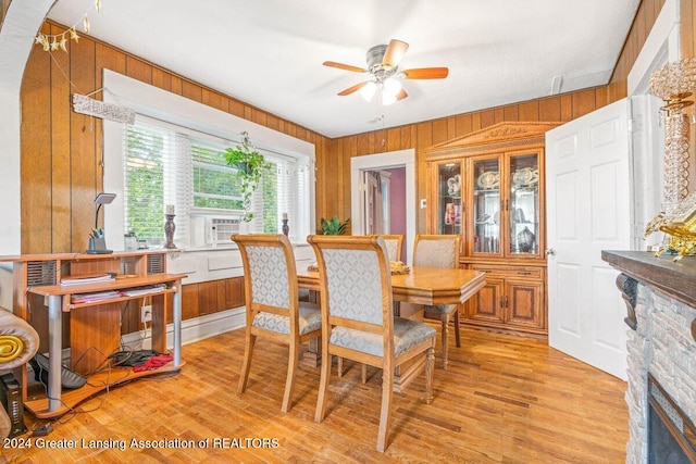 dining space featuring a stone fireplace, wooden walls, ceiling fan, and light wood-type flooring