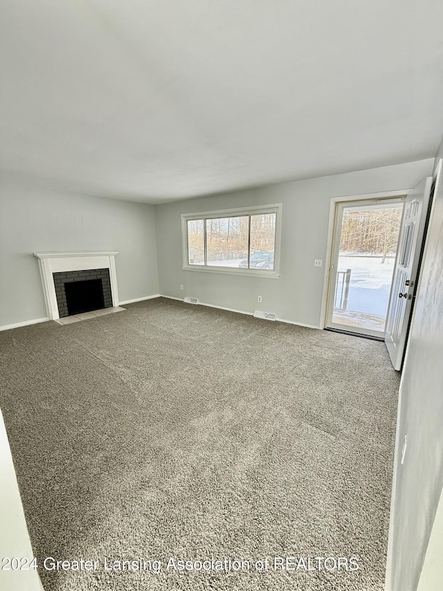 unfurnished living room featuring carpet, a brick fireplace, and plenty of natural light