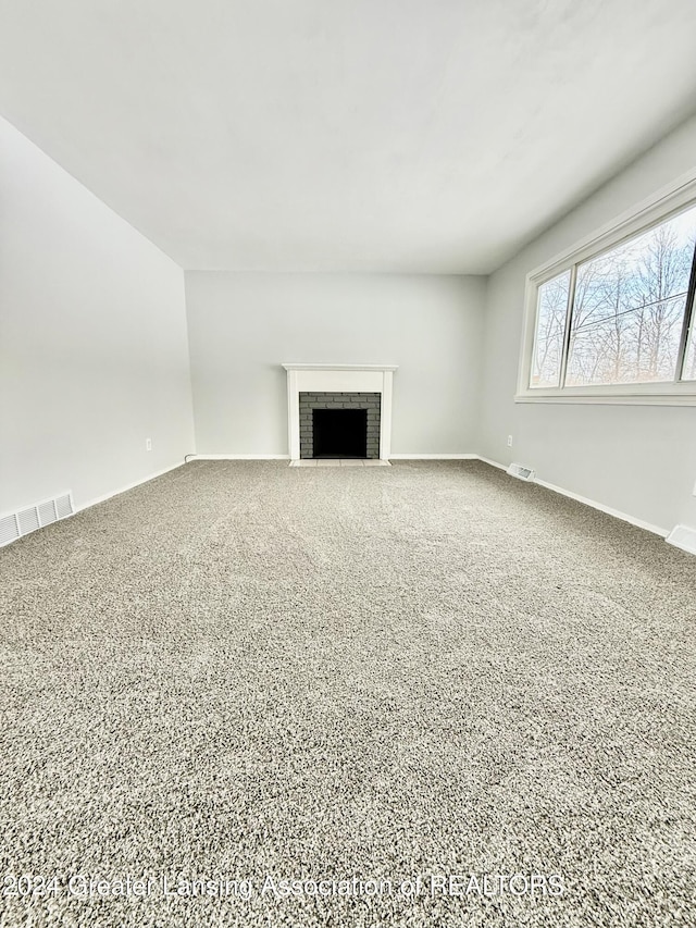 unfurnished living room featuring carpet floors and a brick fireplace