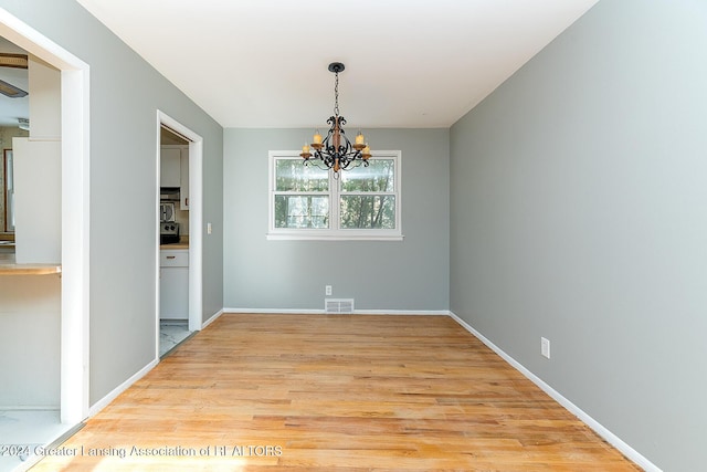 unfurnished dining area featuring light wood-type flooring and an inviting chandelier