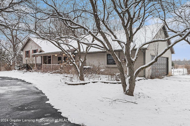 snow covered rear of property with covered porch and a garage