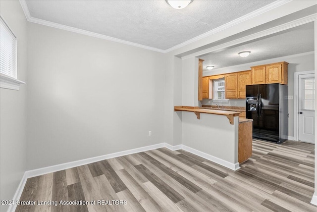 kitchen featuring black refrigerator with ice dispenser, kitchen peninsula, crown molding, a textured ceiling, and a kitchen bar