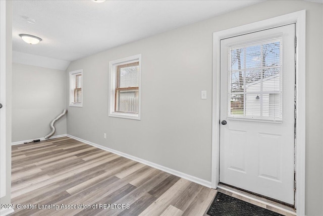 doorway featuring plenty of natural light, light hardwood / wood-style floors, a textured ceiling, and vaulted ceiling