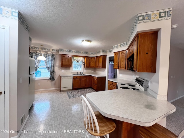 kitchen with a textured ceiling, dishwasher, a kitchen bar, electric stove, and kitchen peninsula