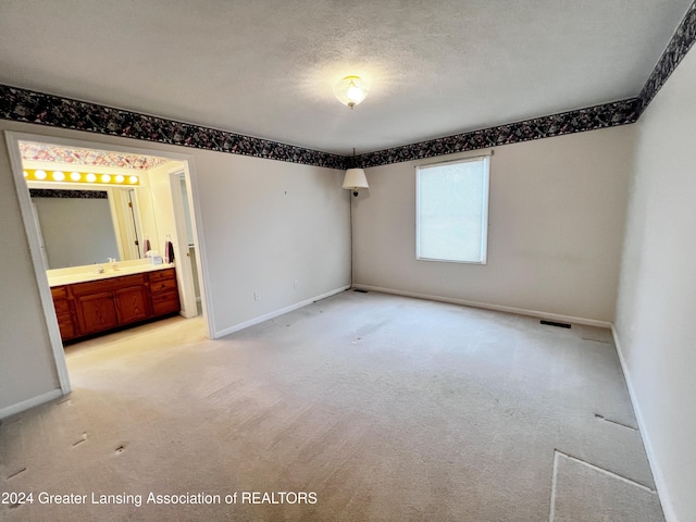 unfurnished bedroom featuring a textured ceiling, ensuite bathroom, light colored carpet, and sink