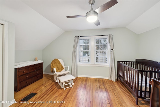 bedroom featuring a crib, vaulted ceiling, light hardwood / wood-style flooring, and ceiling fan